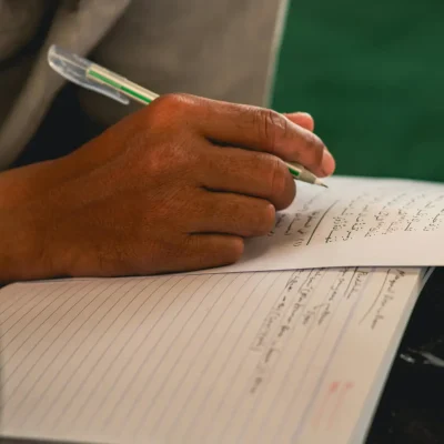 Apprenant arabe étudiant avec cahier, livres et ordinateur, pratiquant la lecture, l’écriture, les dialogues et la grammaire.